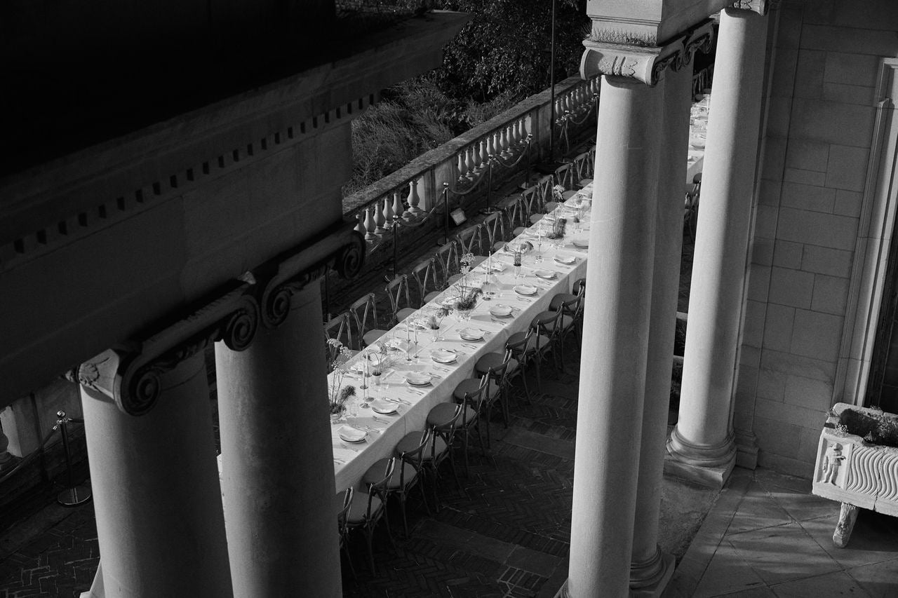 Long dinner table set on the brick terrace, seen from above between the stone columns of Alder Manor