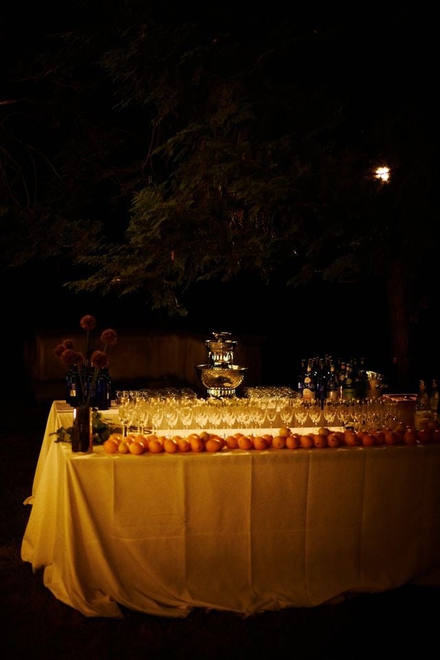 Outdoor bar at night under the trees, with rows of glasses and oranges on a white tablecloth